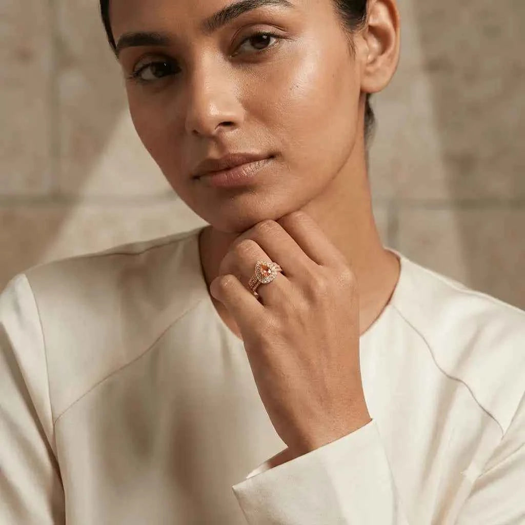 gehna official rose gold plated ring featuring a pear-shaped golden stone surrounded by zircon on a woman's finger.
